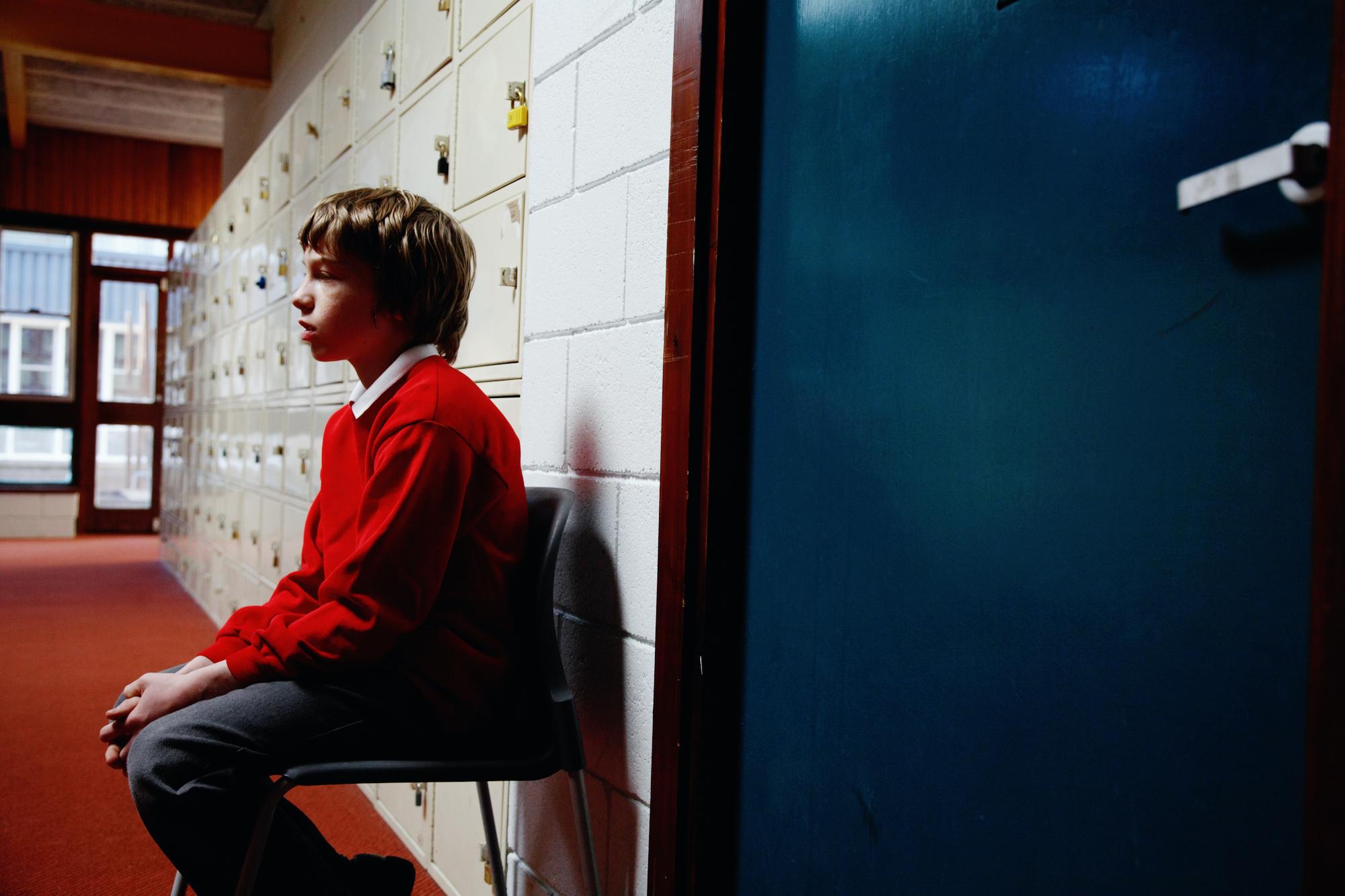 schoolboy sitting on chair in corridor